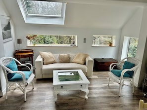 Un salon chaleureux avec un canapé, deux fauteuils en osier blancs, une table basse et une lucarne.