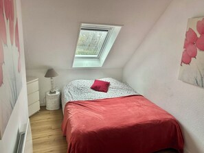 A bedroom with a sloped ceiling, a skylight, a bed with a red blanket, a bedside lamp, and a small round table. - Quiet vacation home in the dunes of Le Touquet, 2 bedrooms, 5 minutes from downtown (Paris)