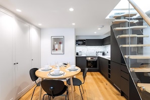 A modern kitchen with a black countertop, white speckled backsplash, and a built-in oven. - Coleherne Road Residence IX (London)