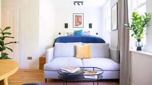Una sala de estar moderna con un sofá gris, una mesa de centro con revistas, una escalera y un ventanal con cortinas.