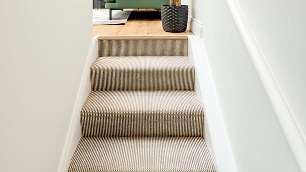 A staircase leading to a living area with a green sofa, a potted plant, and a kitchen in the background.