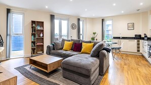 Un salon moderne avec un canapé d’angle gris, une table basse en bois et une bibliothèque.