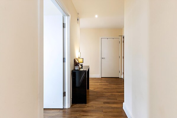 Un pasillo con piso de madera, paredes blancas y una puerta al final.