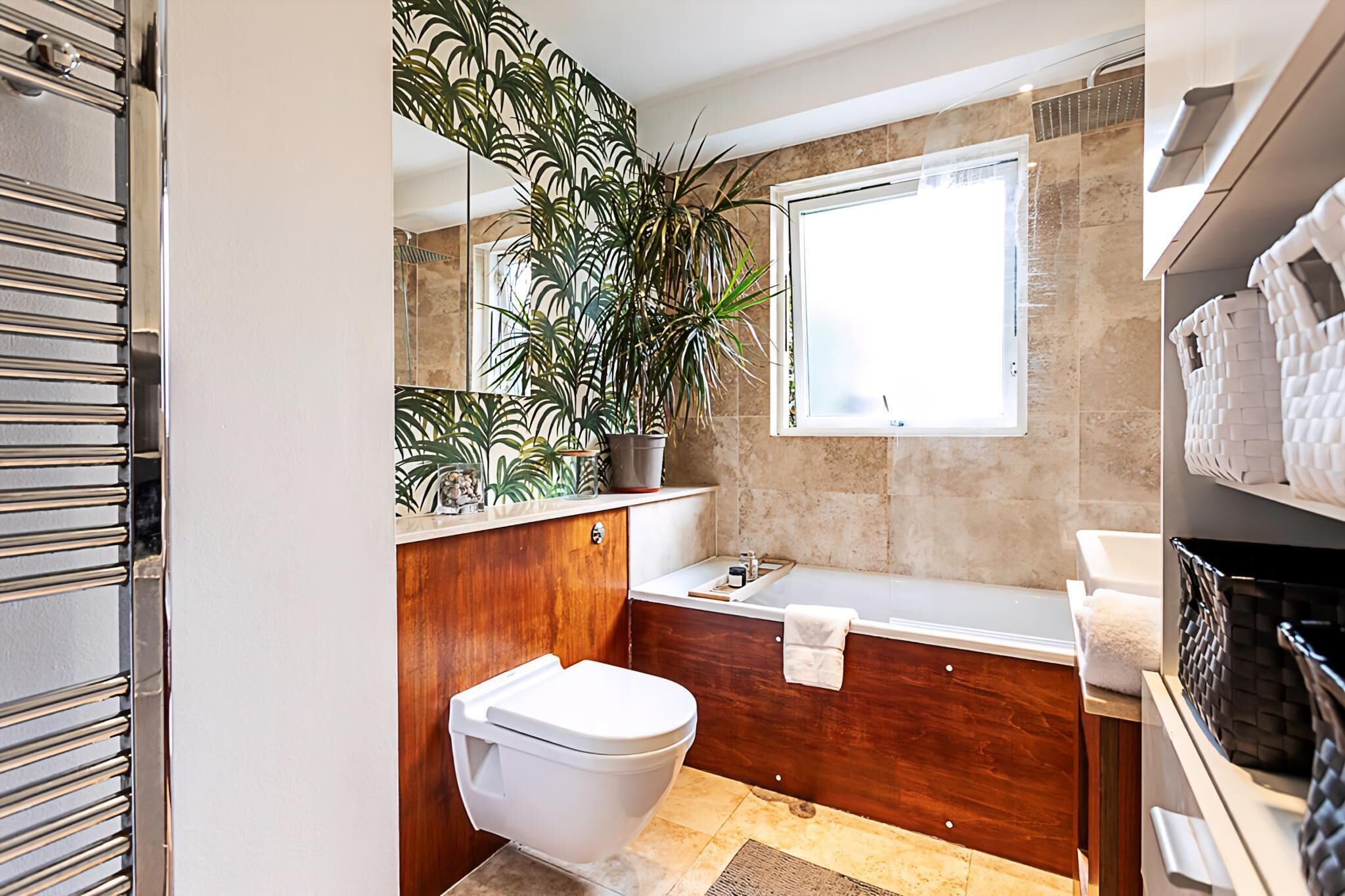 Une salle de bain moderne avec des toilettes, un lavabo et une baignoire, une grande plante en pot et une fenêtre.