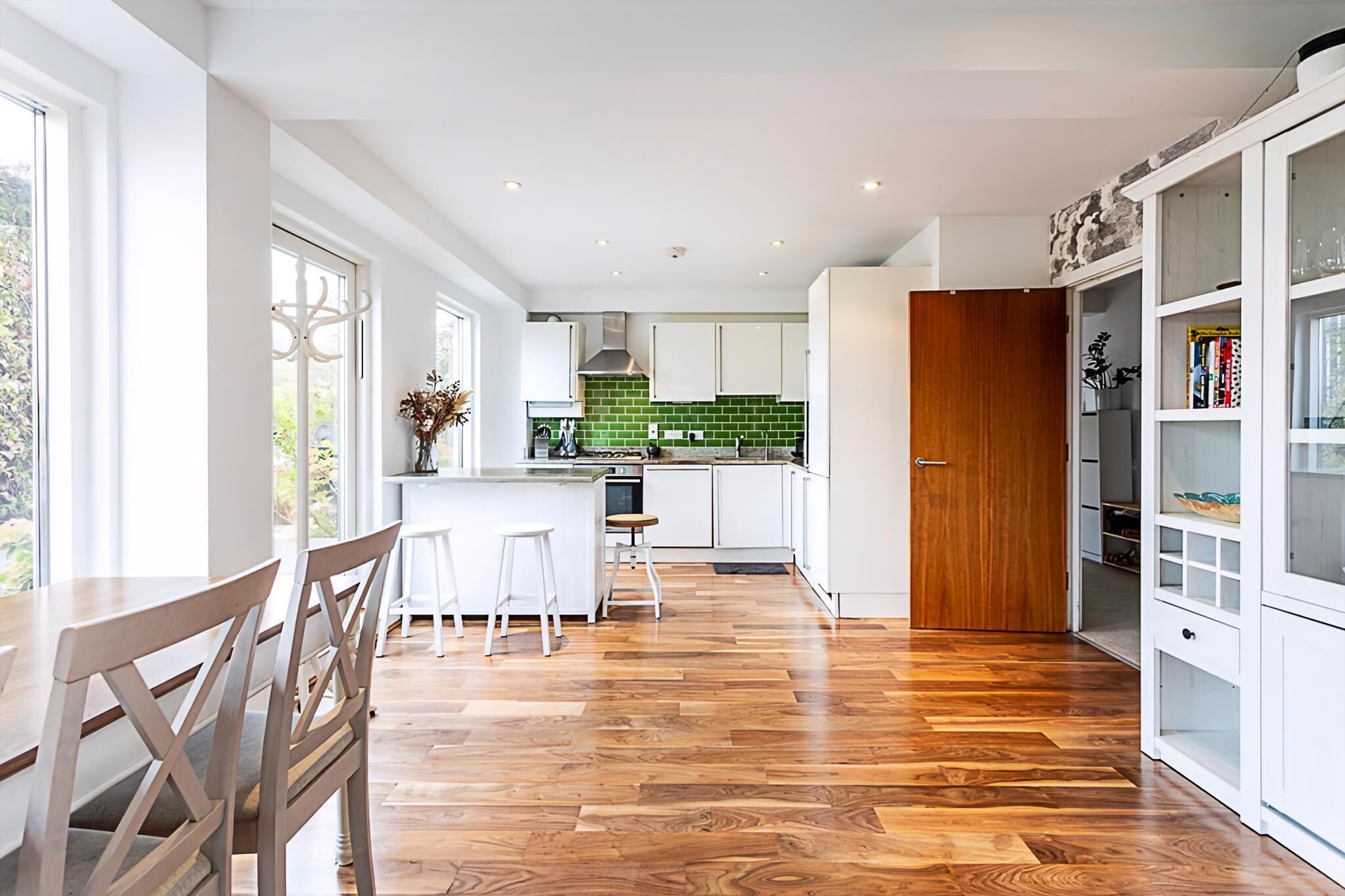 A modern kitchen with white cabinets, a green backsplash, and a wooden floor.