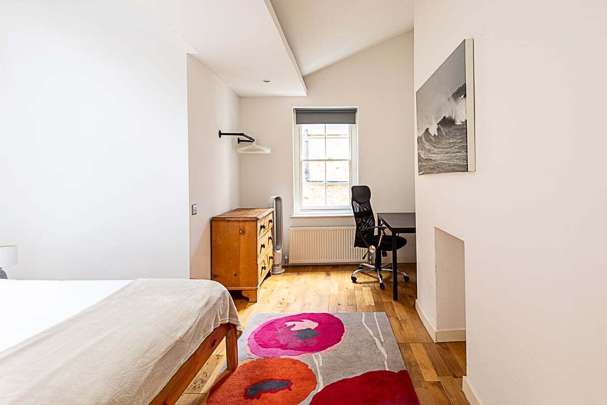 A bedroom with a bed, a wooden dresser, a desk with a chair, a radiator, and a window with a view of the outdoors.