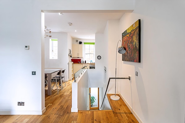 A modern interior with a staircase leading to a dining area, a kitchen with red cabinets, and a painting on the wall. - Farringdon Leo Loft (London)
