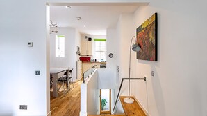 A modern interior with a staircase leading to a dining area and kitchen, featuring white walls and wooden flooring. - Farringdon Leo Loft (London)