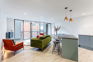 A modern living space with a green sofa, orange armchair, and a kitchen area with a bar stool.