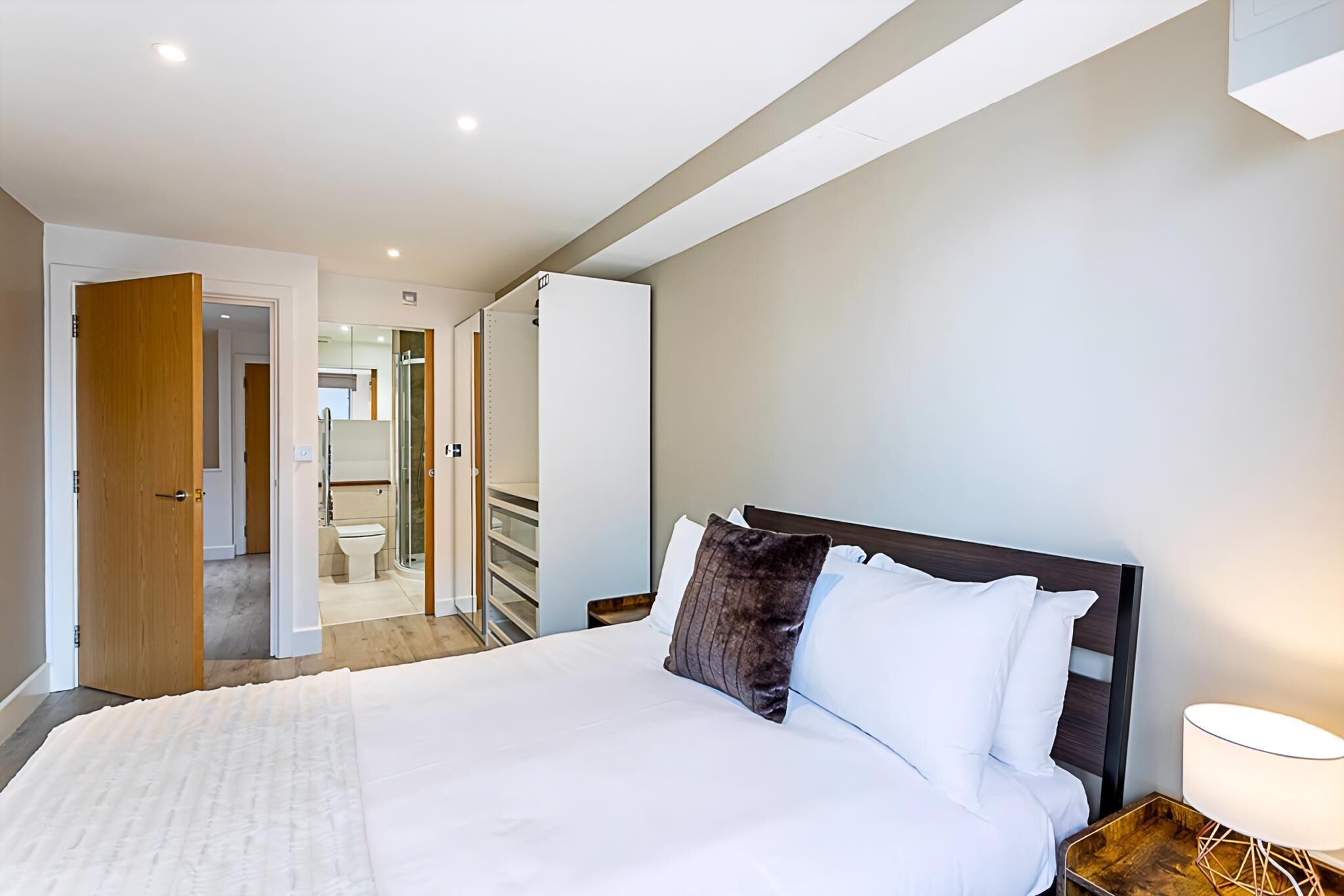 A hotel room with a large bed, a wooden nightstand, and a bathroom visible through an open door.