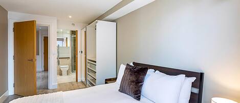 A hotel room with a large bed, a wooden nightstand, and a bathroom visible through an open door.