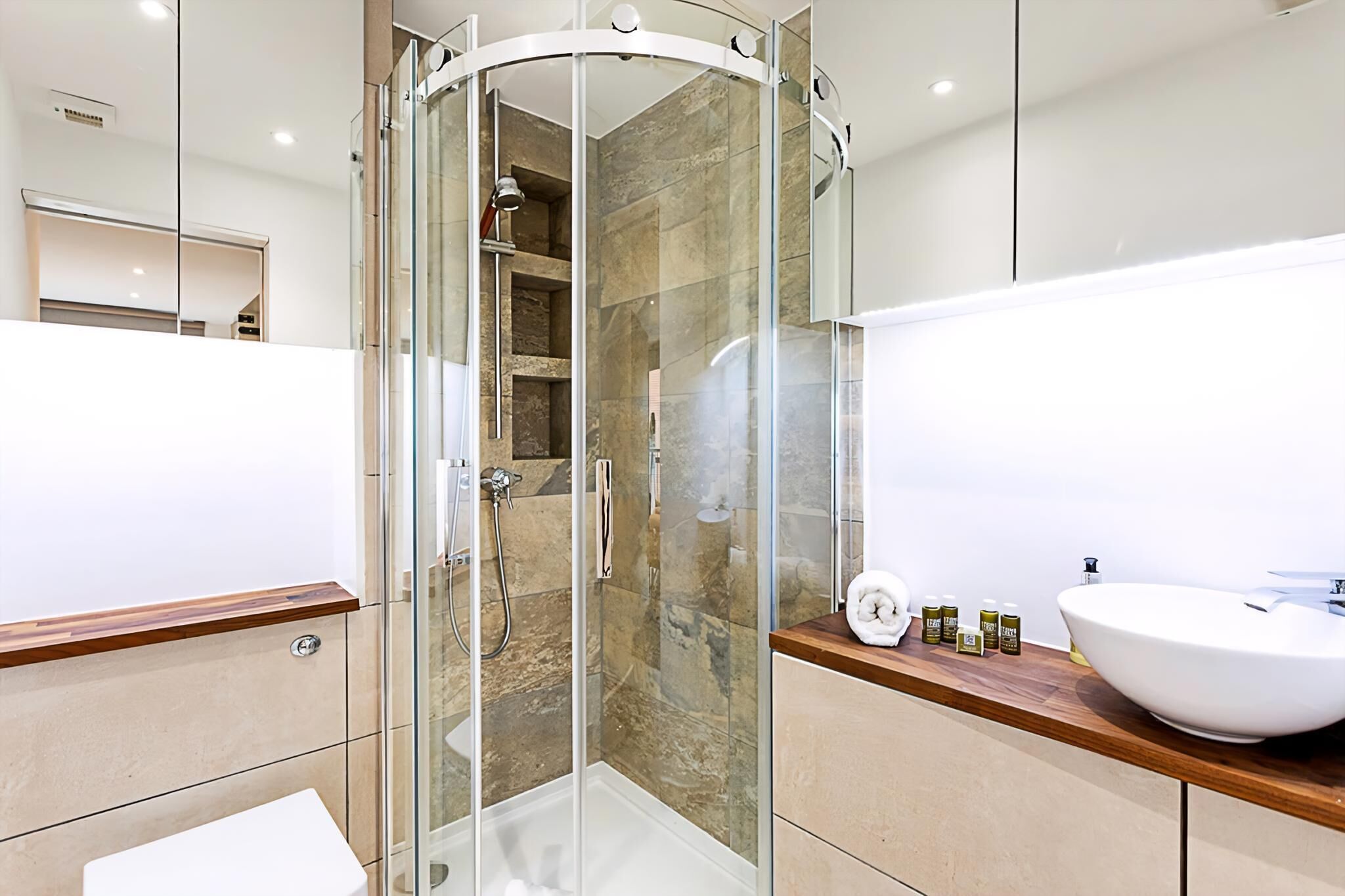 Un baño moderno con ducha de vidrio, un lavabo blanco y encimera de madera.