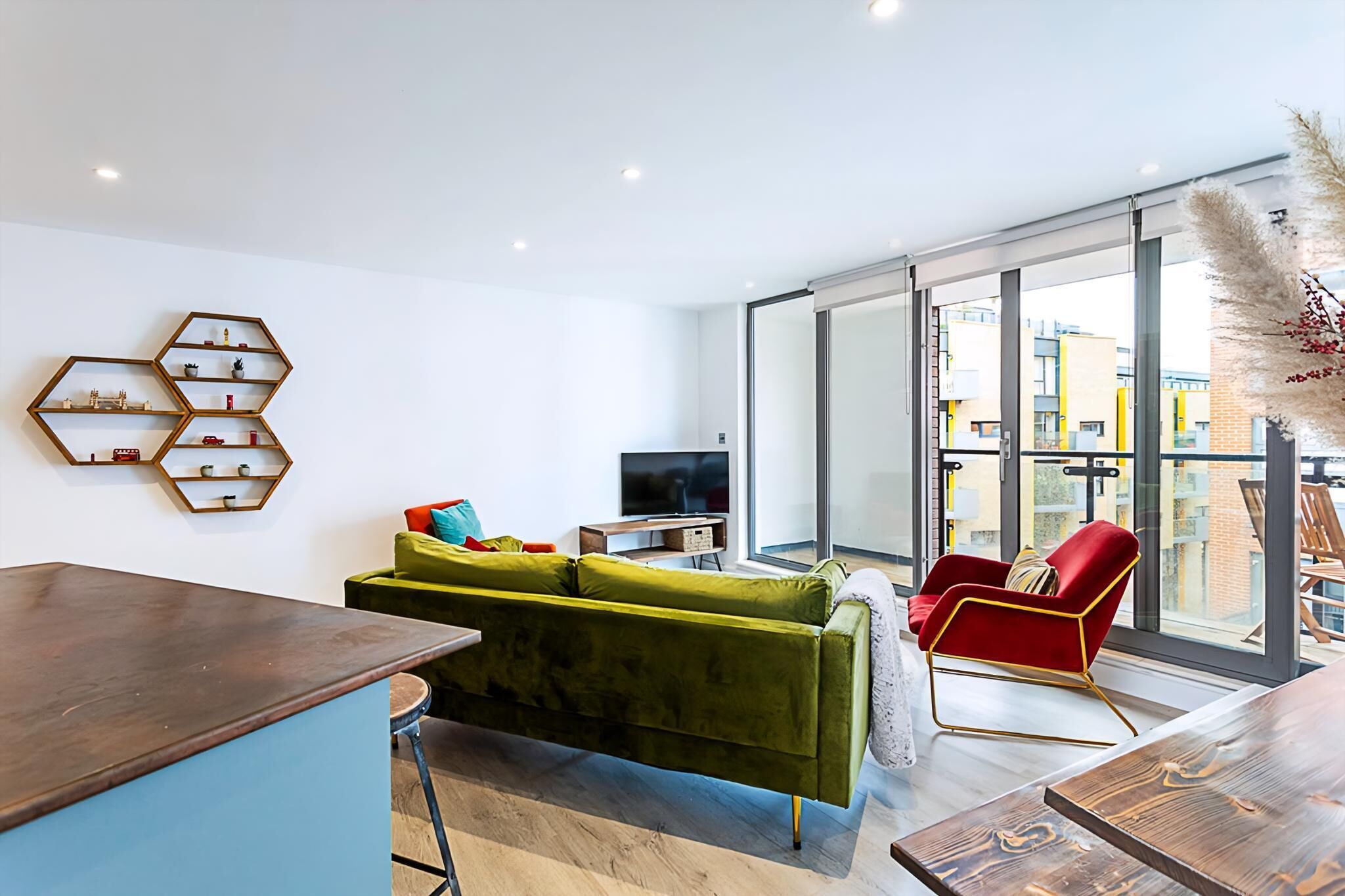 Een moderne woonkamer met een groene bank, een rode fauteuil en honingraatvormige schappen aan de muur.