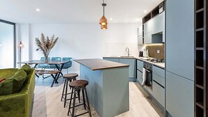 A modern kitchen with a central island, bar stools, a dining area with a table and chairs, and a green sofa. - Duplex Two-bed Apartment Near Tower Bridge (London)