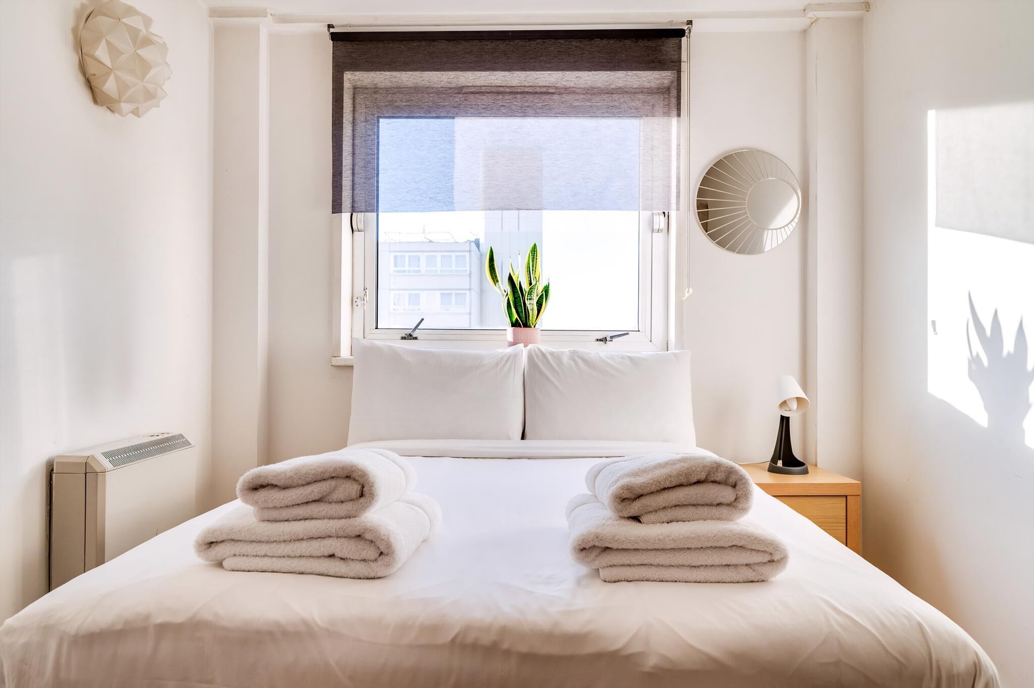 A neatly made bed with folded towels, a potted plant, and a bedside lamp.