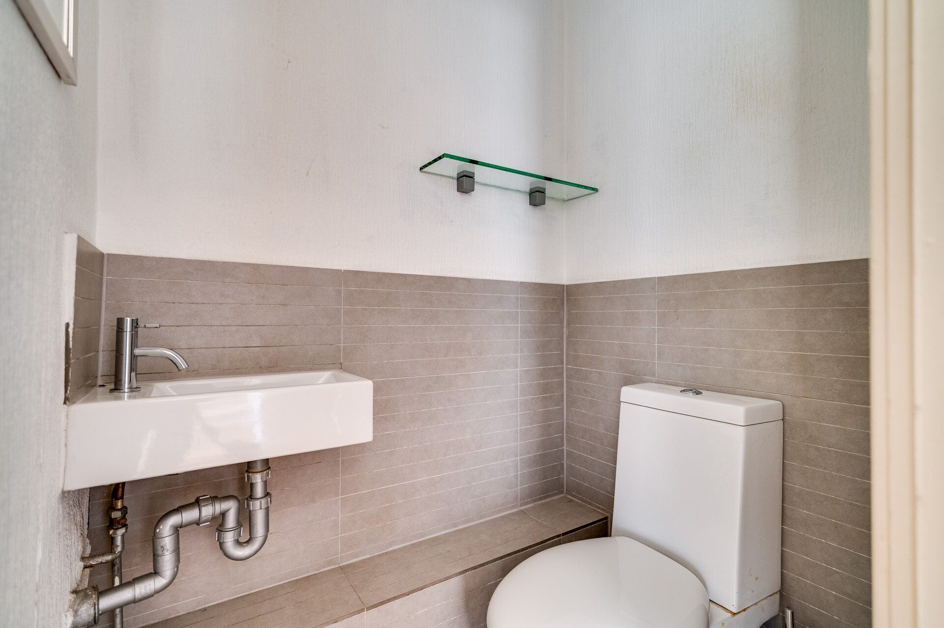 A small bathroom with a white sink, a toilet, and a green shelf above the sink.