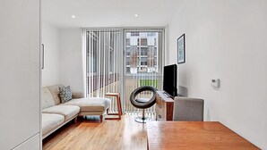 Una sala de estar moderna con un sofá, una mesa de centro, un televisor y vistas de un edificio a través de un ventanal corredero.