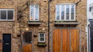 A brick building with a black door, a window with a white frame, and a wooden door. - Beautiful Three Bedroom House in West London (London)