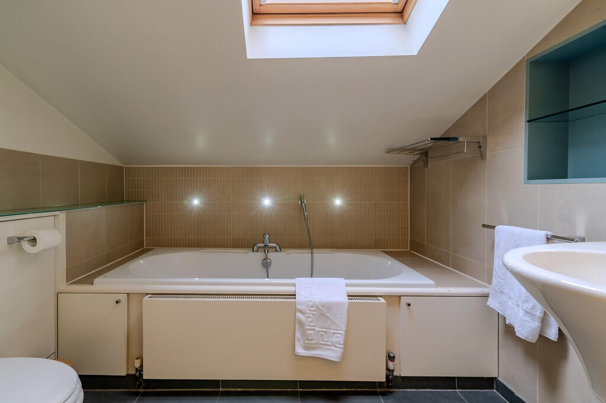 A modern bathroom with a skylight, a bathtub, a sink, and a toilet.