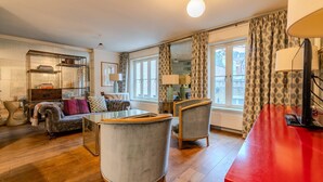 A cozy living room with a sofa, armchairs, a coffee table, and a red table. There are windows with patterned curtains and a mirror on the wall. - Beautiful Three Bedroom House in West London (London)