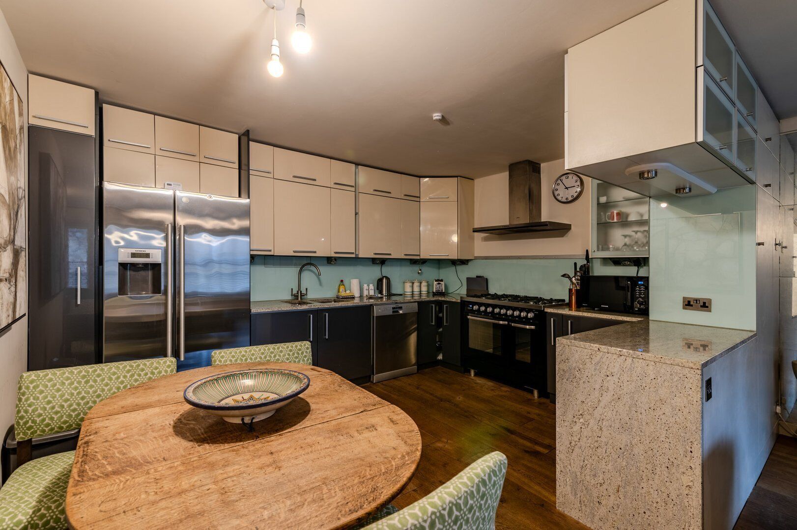 A modern kitchen with a central island, stainless steel appliances, and a dining area with a wooden table and patterned chairs.