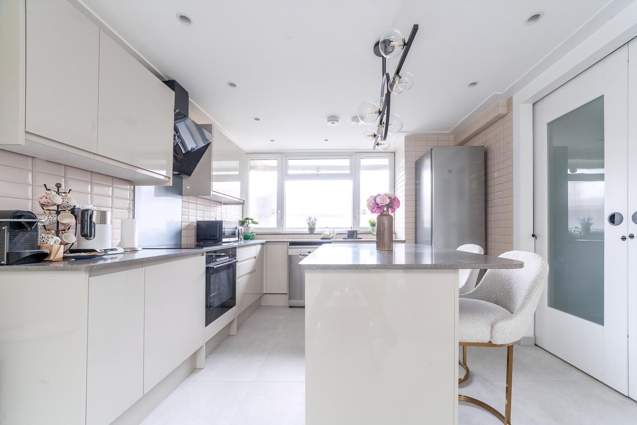 A modern kitchen with white cabinetry, a central island, and a large window providing natural light.