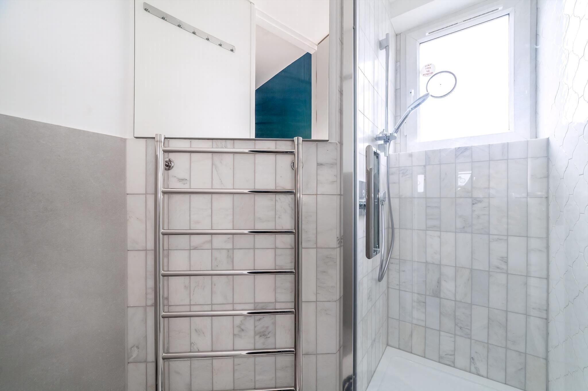 A bathroom with a shower, a towel rack, and a window.