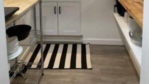 A compact kitchen with white cabinets, a black and white striped rug, and a hanging knife rack.