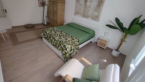 A bedroom with a bed, a wooden wardrobe, a green sofa, a potted plant, and a small table with a lamp. - The Green Arch, located in the center of the seaside village of San Nicola l'Arena (San Nicola l'Arena)