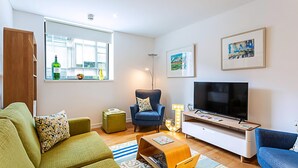 A modern living room with a sofa, armchair, TV, and a small table. - Perfect Paddington Pad (London)