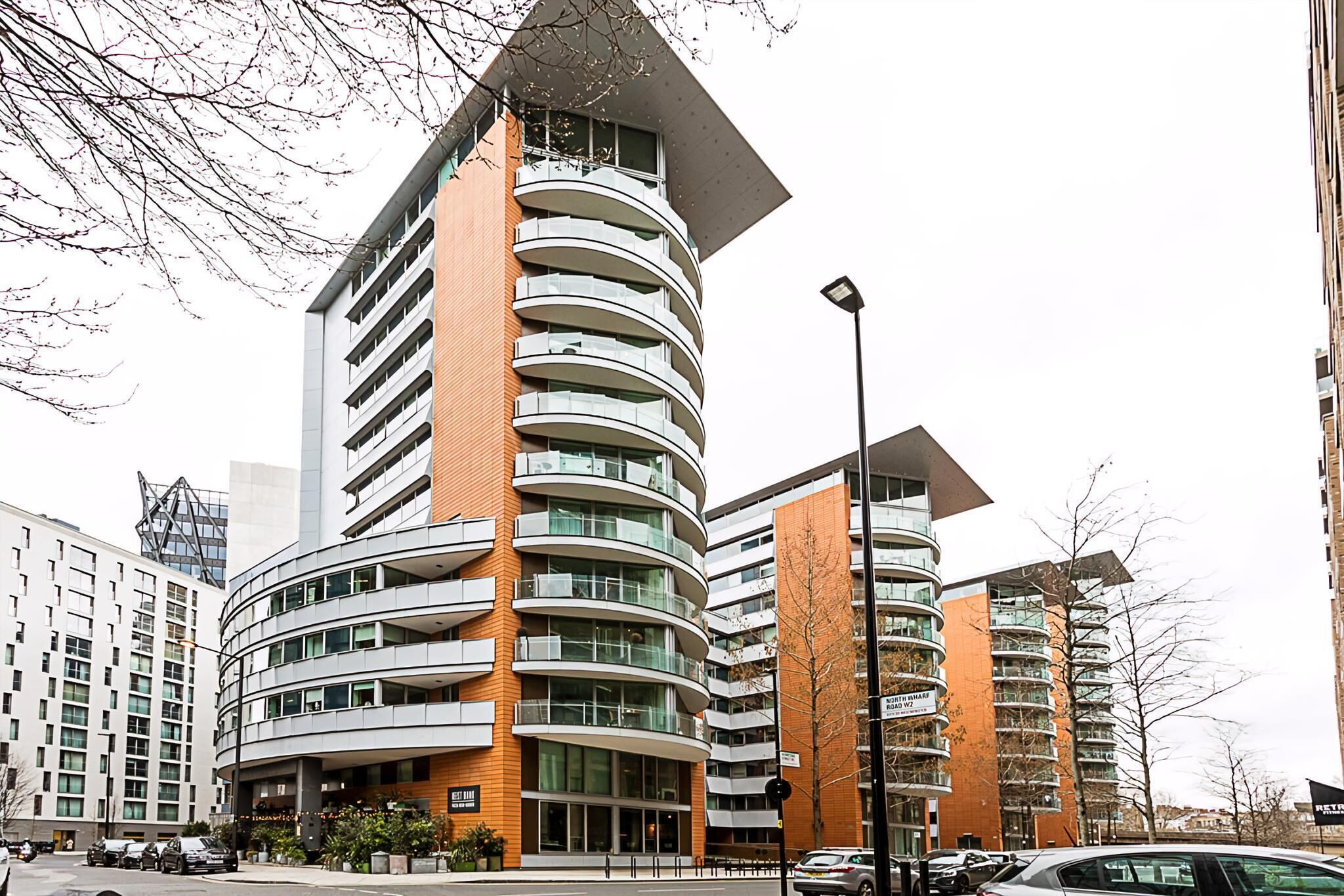 A modern multi-story building with a curved facade, multiple balconies, and a mix of glass and brick materials.