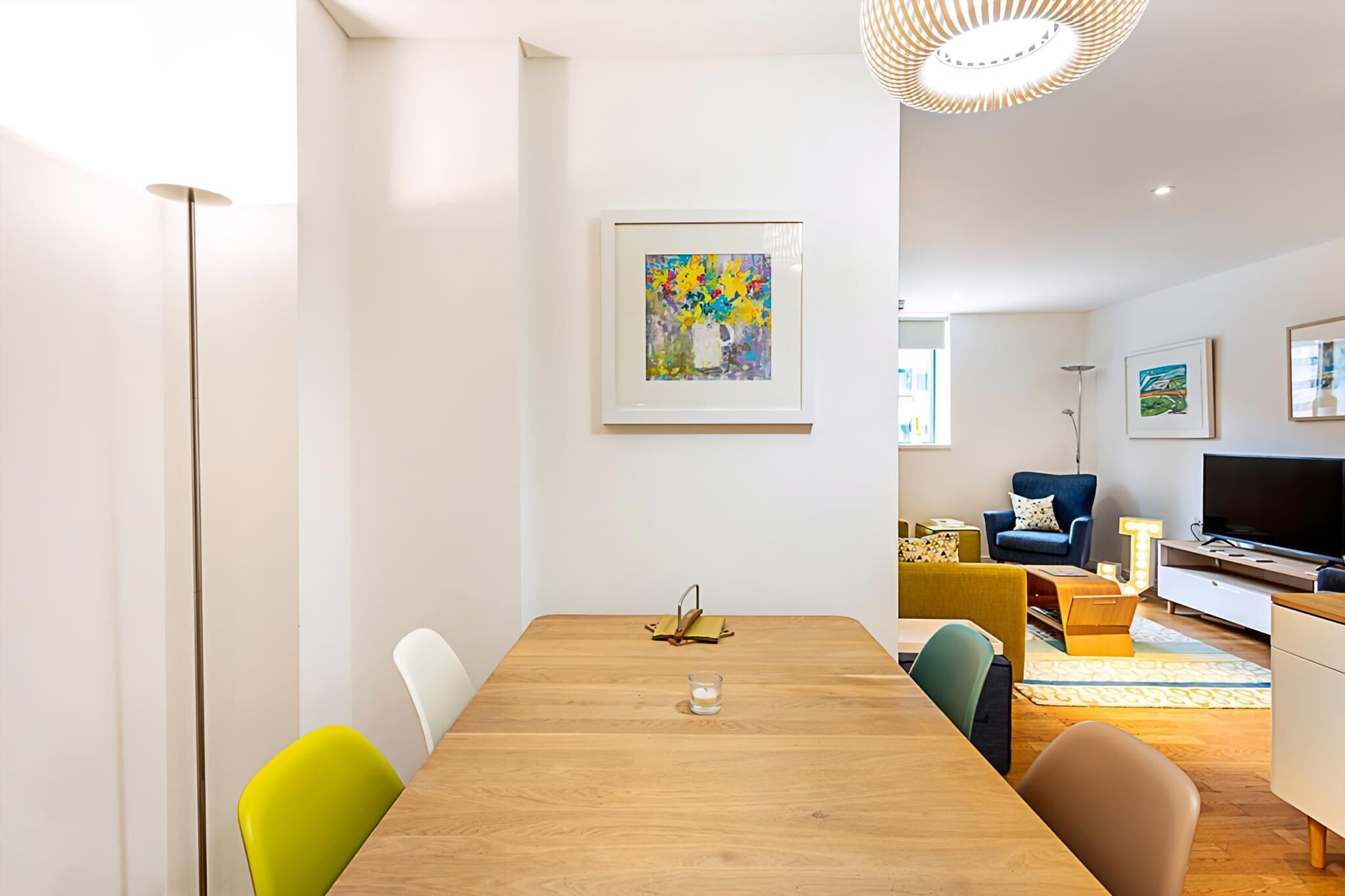 A modern living room with a wooden dining table, colorful chairs, a sofa, and a TV.