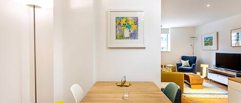 A modern living room with a wooden dining table, colorful chairs, a sofa, and a TV.
