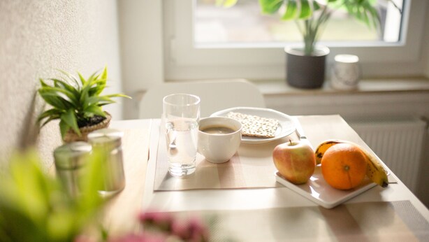 Ein Frühstückstisch mit einem Teller Essen, einem Glas Wasser, einer Tasse Kaffee und einer Topfpflanze.
