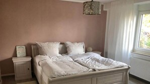 Ein Schlafzimmer mit einem Bett, Nachttischen, einer Lampe und einem Fenster mit Vorhängen.