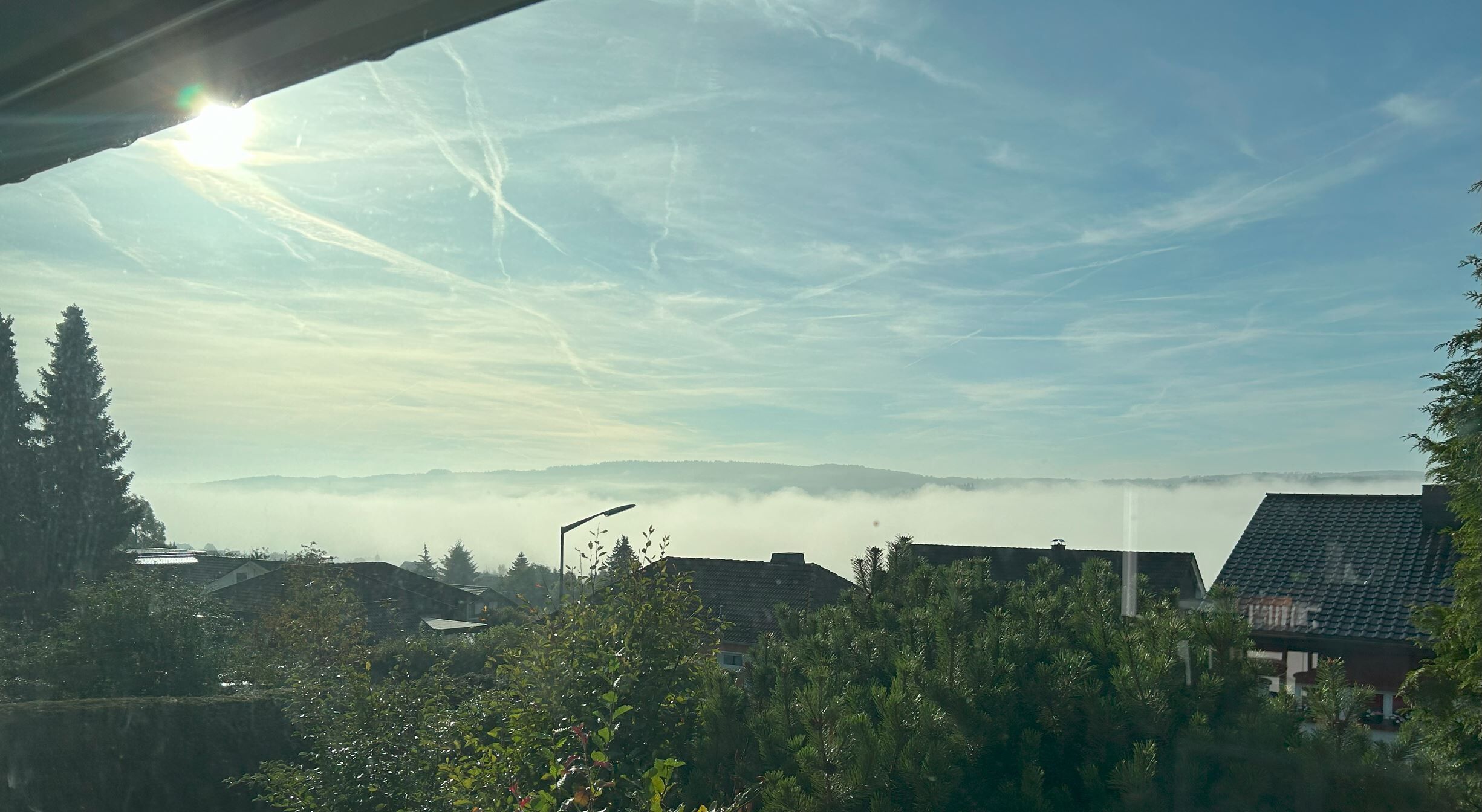 A residential area with houses, trees, and a clear sky with clouds.