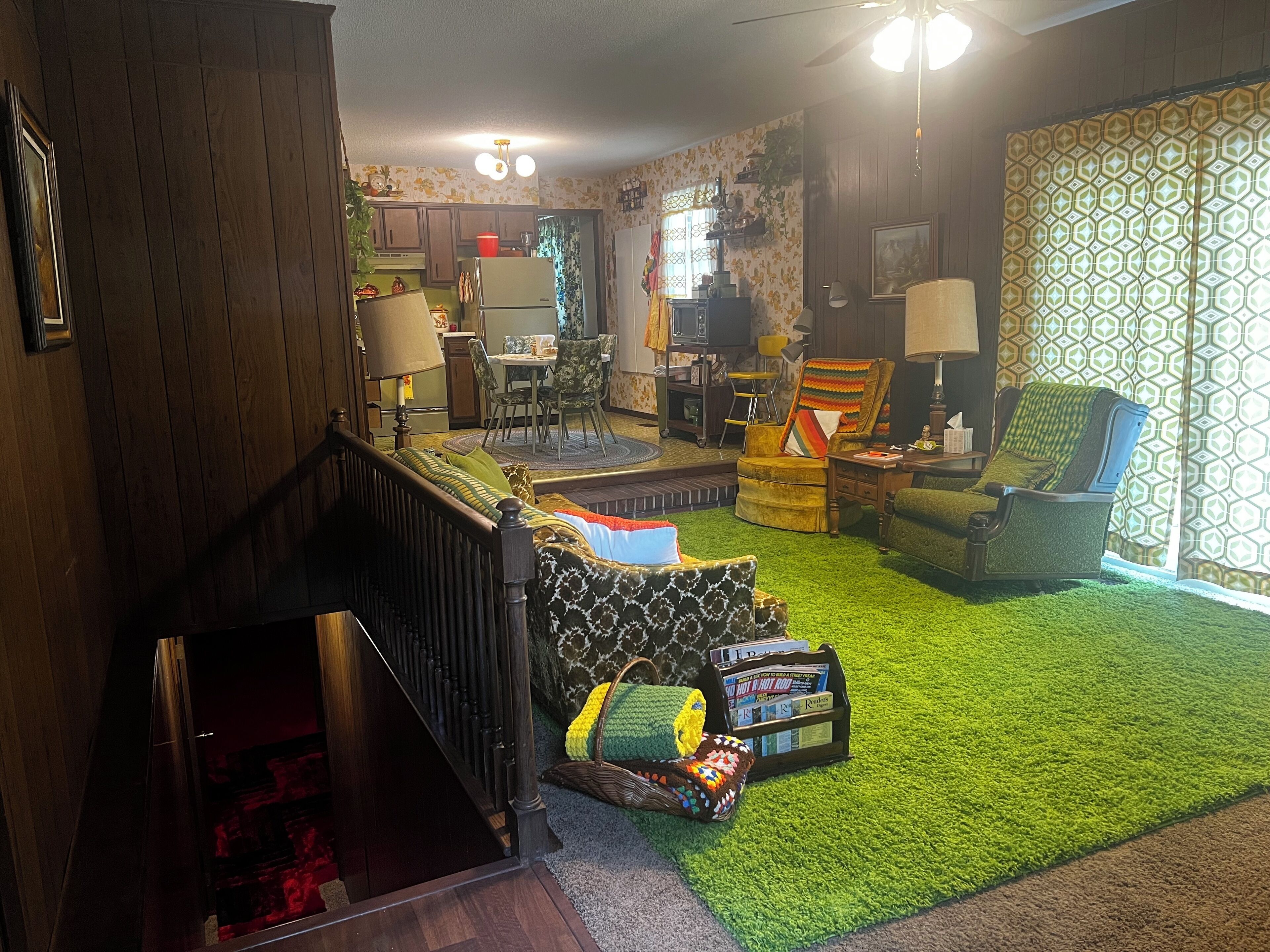 Un salon chaleureux avec un escalier, un coin repas et une cuisine en arrière-plan.