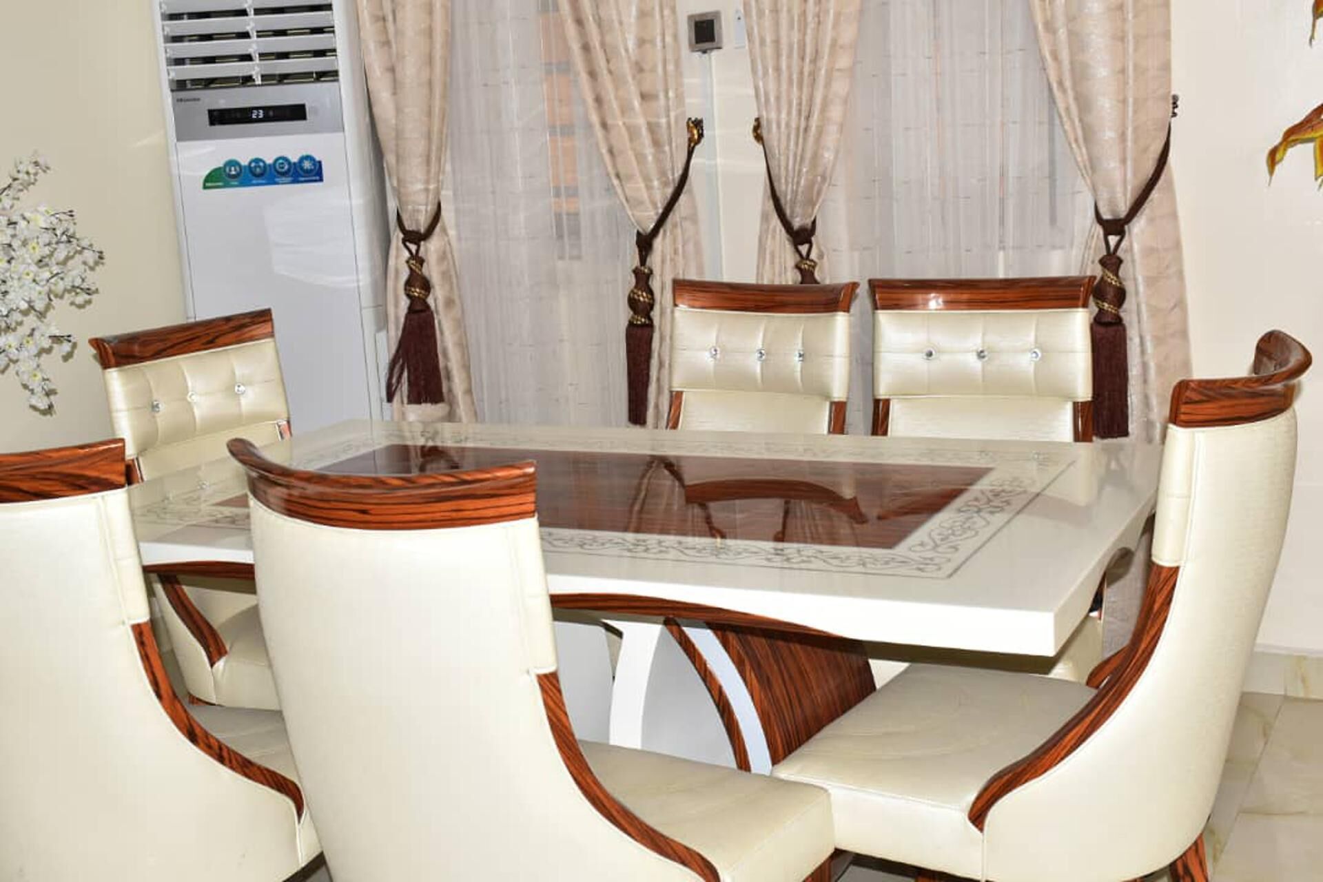 A dining area with a glass-top table surrounded by six upholstered chairs with wooden accents.