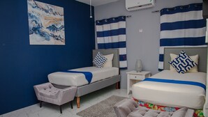Un dormitorio con dos camas, una decoración en tonos grises y blancos, cortinas a rayas y suelo de mármol.