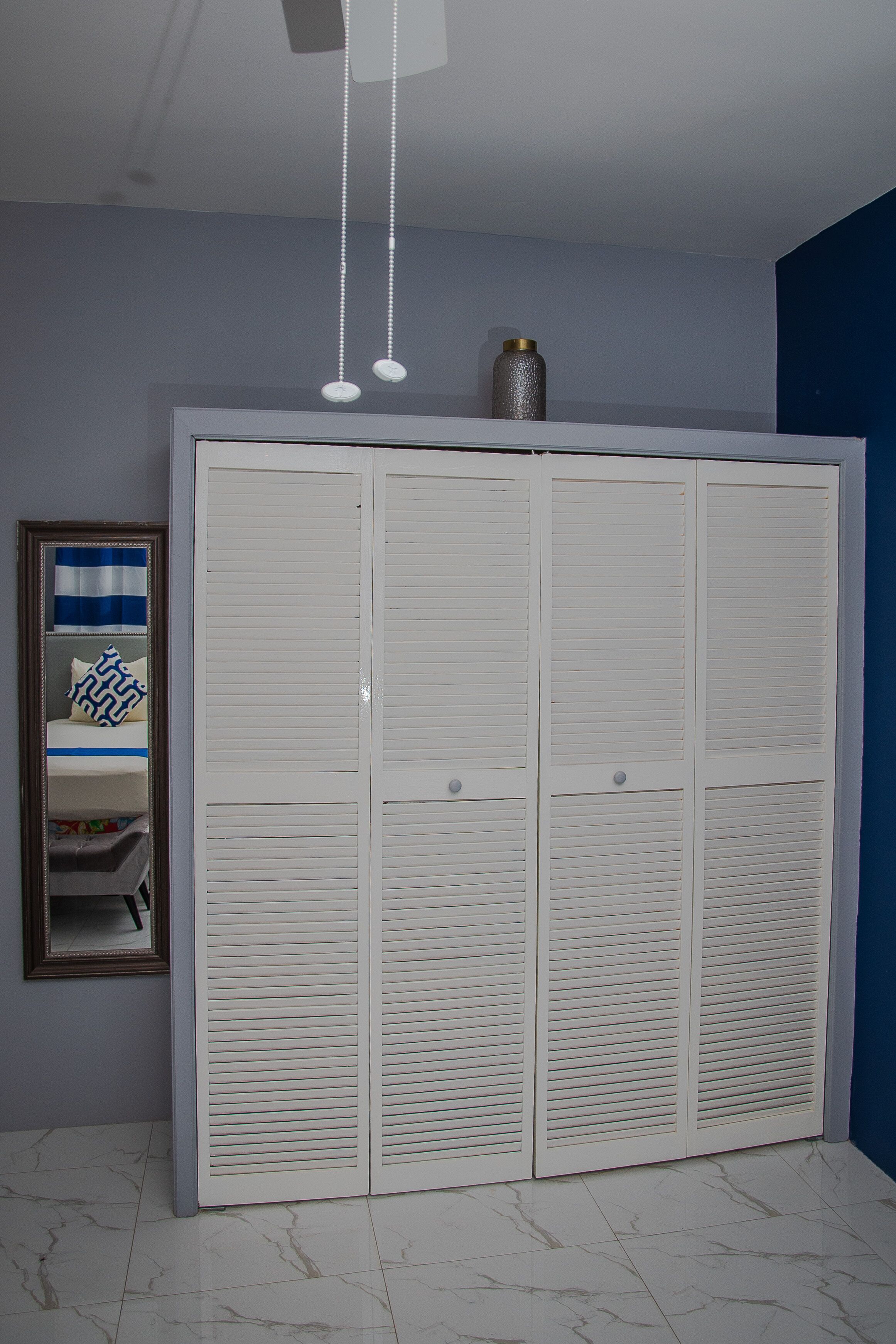 A room with a white wardrobe, a mirror, and a bed with blue and white bedding.