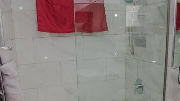 A glass-enclosed shower with a handheld showerhead, a toilet, and a pink rug.