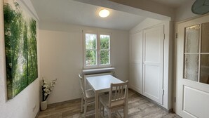 A dining area with a table and chairs, a window with a view of greenery, and a door with frosted glass panels. - Ruhig und Idyllisch: Kleines Ferienhaus am Waldrand - S-bahn-nähe - Zentrumsnah (Bergisch Gladbach)