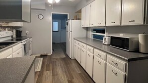 A kitchen with white cabinets, a microwave, a refrigerator, and a ceiling fan.