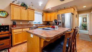 A kitchen with wooden cabinets, a stainless steel refrigerator, a clock, and a dining area with chairs.