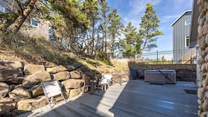 A wooden deck with outdoor furniture, a stone wall, and a house in the background.
