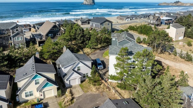 A coastal residential area with houses, a clear view of the ocean, and a prominent rock formation.
