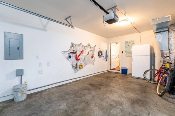 A spacious room with a concrete floor, a white wall with a net art installation, a white refrigerator, and a bicycle.