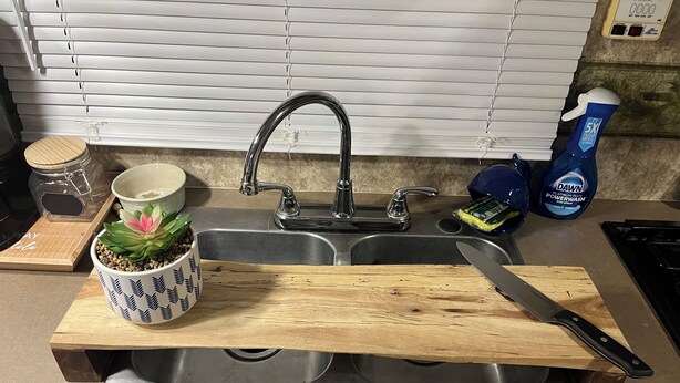 A kitchen with a wooden cutting board, a knife, a sink, and a potted plant. - Cozy little camper, nestled quietly in the country / only minutes from the city  (Purvis)