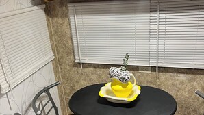 A compact kitchen with wooden cabinets, a black table, two chairs, a woven rug, and a window with blinds. - Cozy little camper, nestled quietly in the country / only minutes from the city  (Purvis)