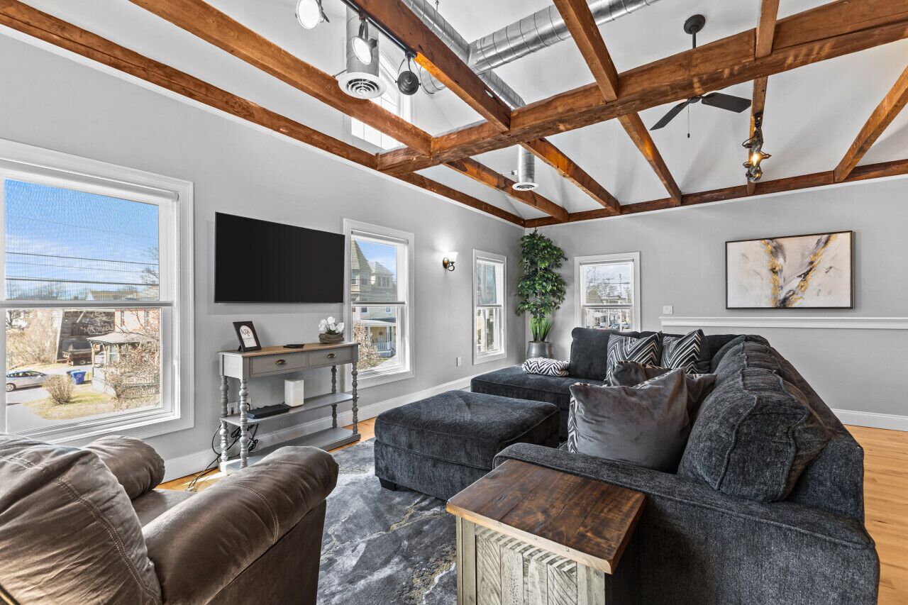 A living room with a large sectional sofa, a wooden coffee table, and a flat-screen TV mounted on the wall.